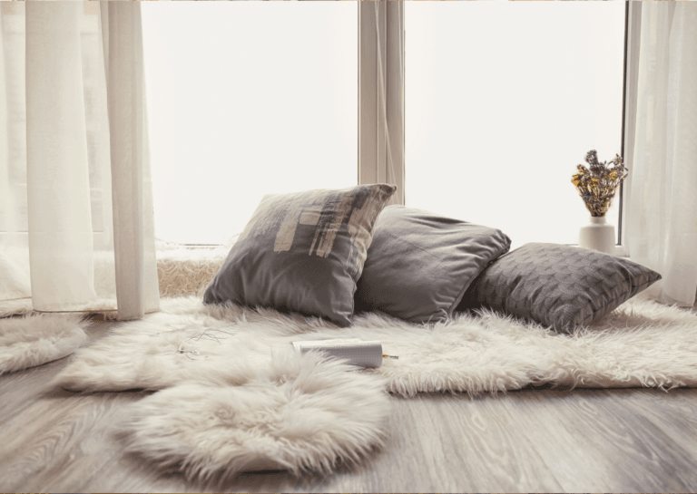 Light-colored, high-pile rectangular rug with a smaller fluffy round rug in front, positioned by a sunlit window with curtains.