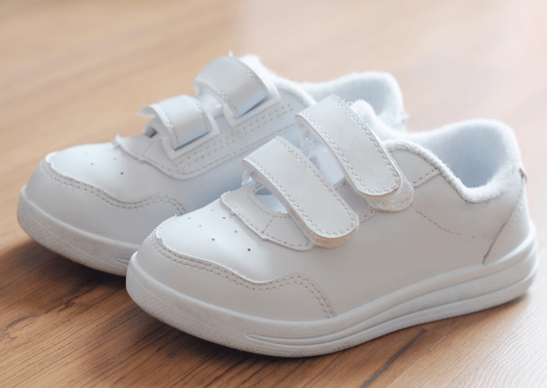 Close-up of pristine white baby shoes on a wooden floor, showcasing their cleanliness and delicate design.