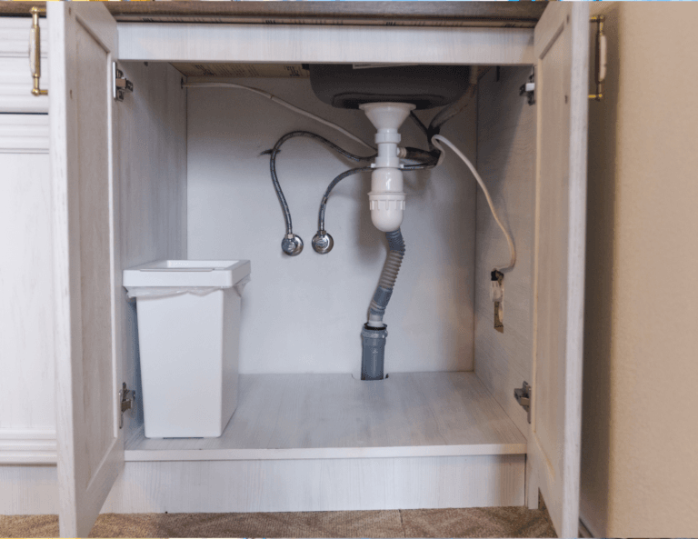 Empty kitchen cabinet under the sink, featuring only a small white trash can, showcasing a clean and organized space.