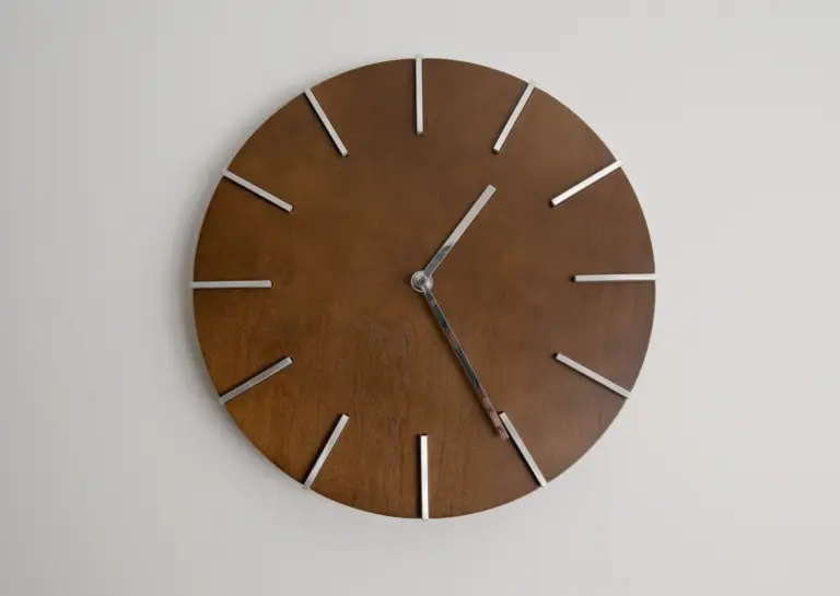 Simple dark brown round wall clock with colorful hands and tick marks, indicating the time as 13:26, against a neutral background.