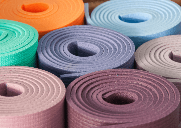 Various yoga mats rolled and standing upright against each other in different colors, showcasing the layered sides of each mat for a vibrant display.