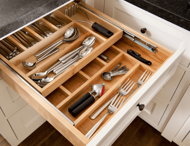 Open kitchen drawer with a two-layered divider neatly organizing various wooden kitchen utensils, creating a tidy and accessible layout.