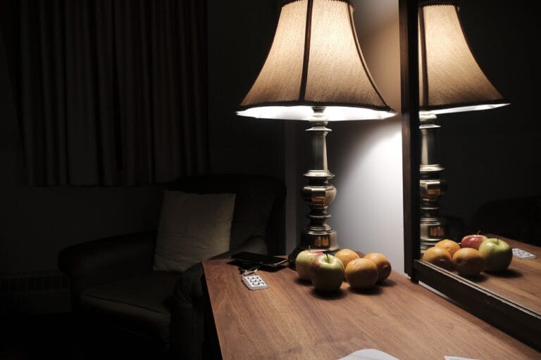 Table lamp turned on atop a dresser in a bedroom, illuminating the dark surroundings.