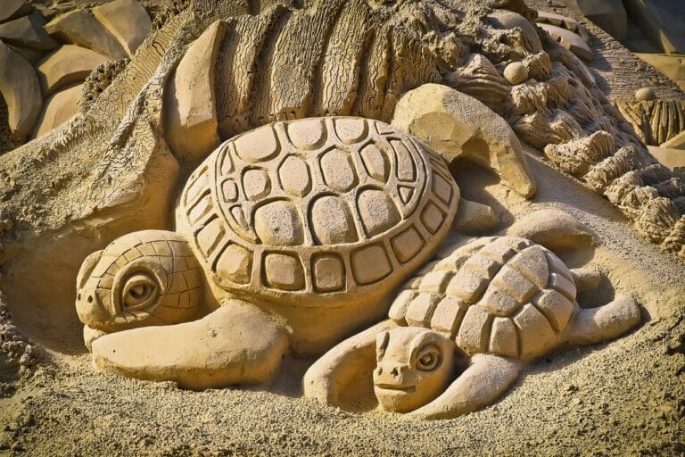 Sand-colored sculpture of two turtles lying in the sand.