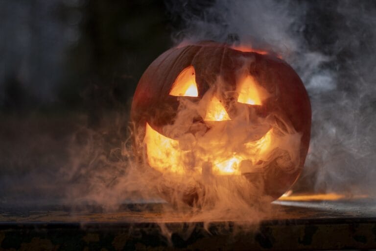 Carved pumpkin with a face, illuminated from within and surrounded by smoke for Halloween.