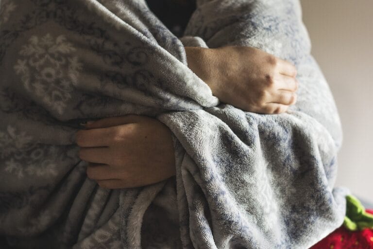 Close-up of a person wrapped in a soft gray blanket, with only their upper body visible.