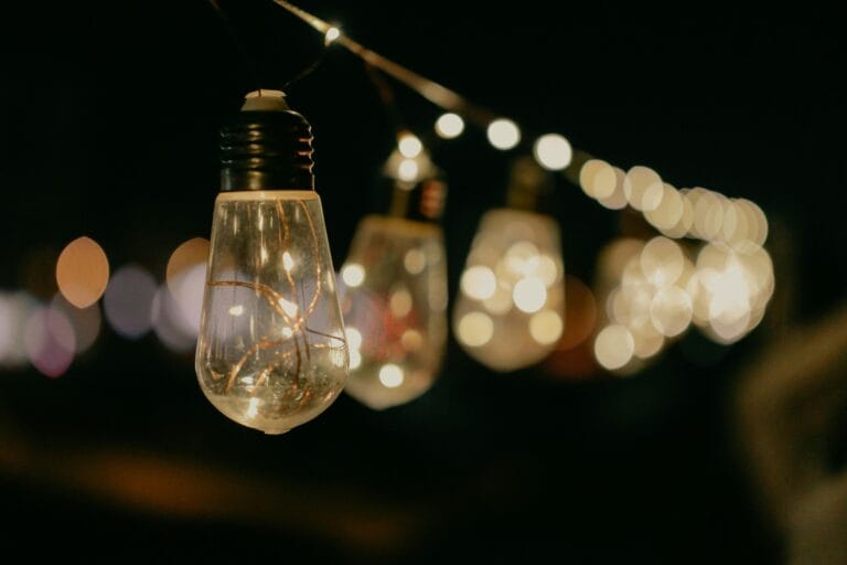 String light bulbs glowing in the dark, hanging outdoors on a cord to create a warm, ambient lighting effect.