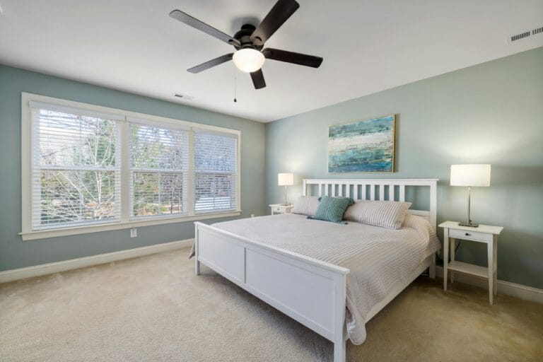 Spacious organized bedroom with ample natural light, featuring mint green walls, a double bed, open blinds, and a ceiling fan.