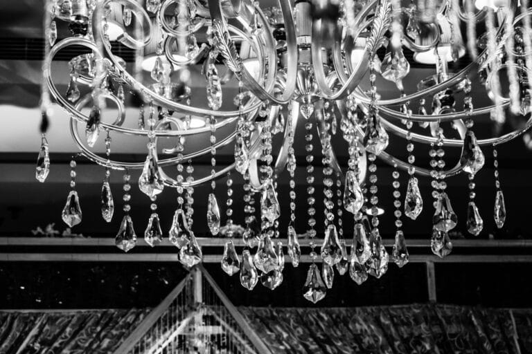 Grayscale Photo of Glass Elegant Chandelier with hanging glass crystals against a dark black background.