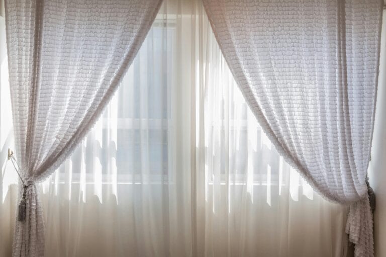 Beige curtain half open with a closed curtain behind it, allowing sunlight to filter through and creating a warm glow.