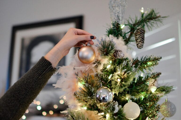 Person Holding Beige Bauble Near Christmas Tree